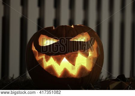 Pumpkin With Glowing Eyes And A Skull On Wooden Background. Sinister Halloween.