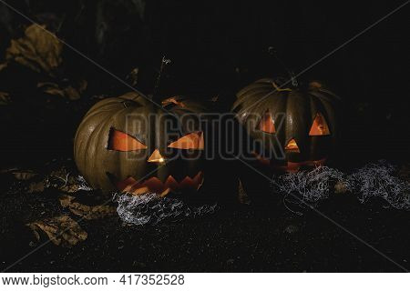 Pumpkin With Glowing Eyes And A Skull On Wooden Background. Sinister Halloween.