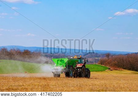 The Tractor Spreads Granular Fertilizer On A Grass Field. Agricultural Work. Mineral Fertilizers. Ni