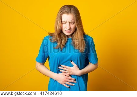 Young Girl Holding Her Stomach And Frowns. Teenage Girl Has A Stomach Ache. Female Writhes In Pain.