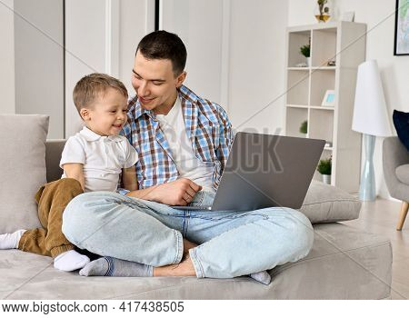 Happy Young Dad And Cute Small Kid Son Using Laptop Computer At Home. Smiling Father Distance Learni