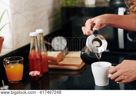 Close-up Image Of Young Woman Pouring Coffee In Cup When Making Herself Breakfast At Kitcen Counter
