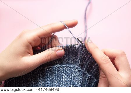 Female Hands With Knitting Needles To Knit Wool Blue Sweater On Pink Background. Woman Knitting Wool
