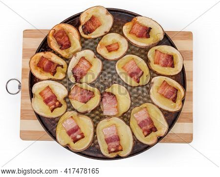 Potato Halves In Their Skins Baked With Bacon Slices On A Round Baking Sheet On Wooden Cutting Board