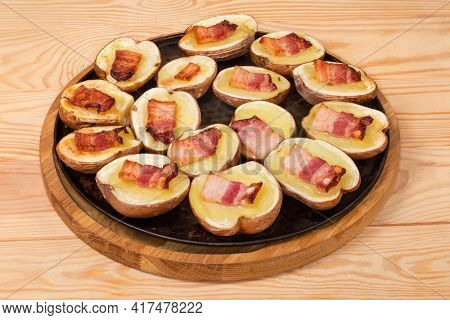 Potato Halves In Their Skins Baked With Bacon Slices On A Round Baking Sheet On A Rustic Table