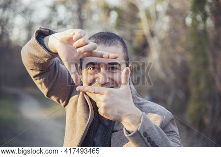 Handsome Man In Coat Folded The Semblance Of A Frame From His Hands In Autumn Park
