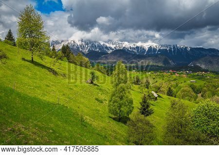 Amazing Summer Countryside Scenery With Green Fields On The Slopes And High Snowy Piatra Craiului Mo