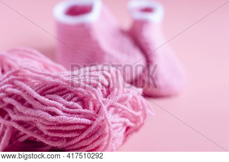 A Ball Of Pink Yarn In The Foreground And Knitted Shoes In The Background Knitting Concept