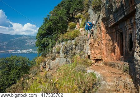 Hiking Lycian way. Man is descending tricky path on cliff high above Mediterranean sea near ancient rock tomb of Saba in Ancient Sites on Lycian way trail, Trekking in Turkey, outdoor activity