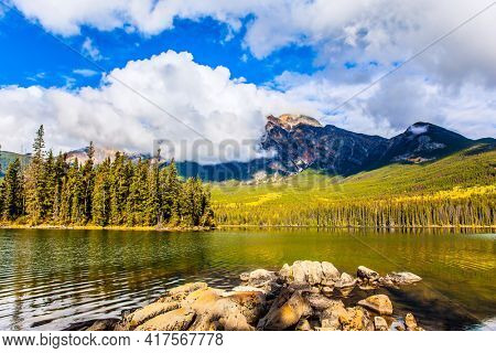 Pyramid Lake. The lake is covered with light water ripples. Cold sunny day in the Rocky Mountains of Canada. Mount Pyramid is covered by cumulus clouds. 