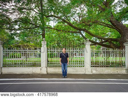 Asian Black T-shirt Is Standing In Front Of White Vintage Fence Beside The Road In The Afternoon Tim