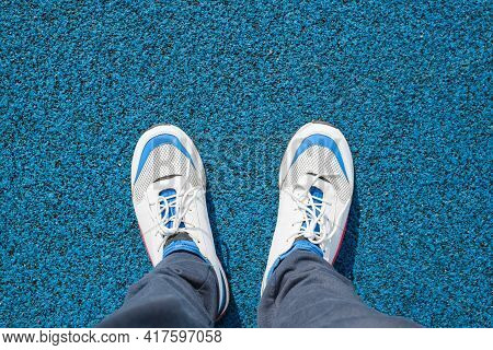 Man In White Running Shoes Stands On A Blue Rubbery Surface Outside, Close-up. Top View, First Perso