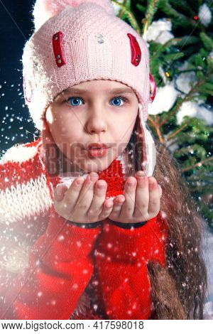 A Girl Child In A Hat With A Pumpon Blows In The Palm Of Her Hand And Snow Flies Out Of Them. A Girl