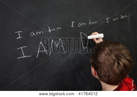 Boy with poor spelling and low self esteem writing on a blackboard