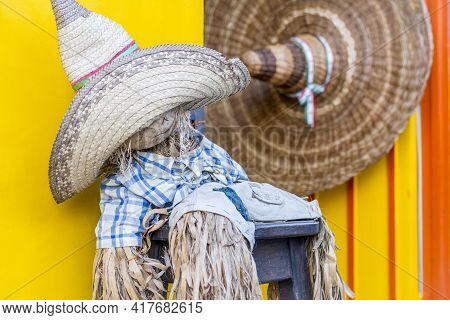 Funny Scarecrow Seated In Front Of A Store With Two Big Hats