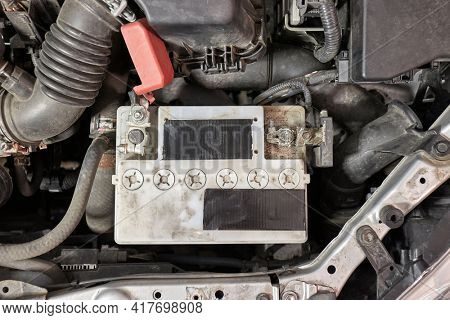 Old car starter battery inside the engine bay viewed from above top down