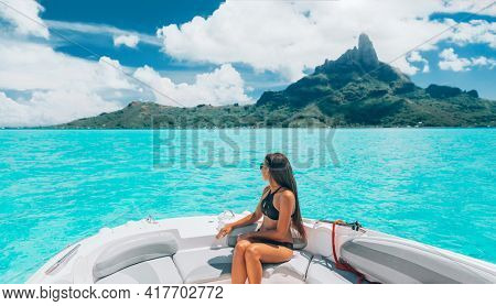 Luxury yacht travel woman enjoying ride on high end speed boat on summer vacation. Elegant black bikini, long hair and sun tanned body. By famous Mount Otemanu, Bora Bora, French Polynesia, Tahiti