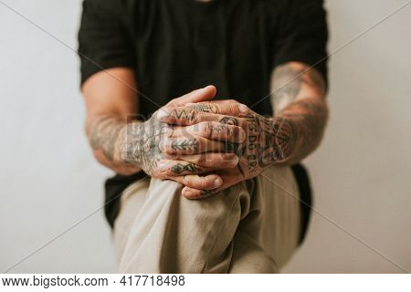 Tattooed man with hands clasping his knees. 2 OCTOBER 2020 - CHIPPENHAM, UK