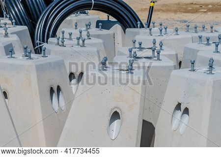 Concrete Bases For Lampposts At Construction Staging Area In Front Of Coils Of Black Pvc Pipe.