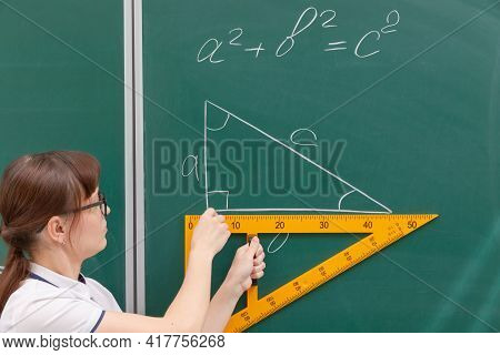 School Teacher Young Woman In The Class At The Blackboard Draws A Triangle With A Ruler. Portrait. C
