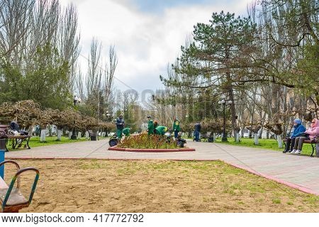 Kerch, Russia - April 2021: Janitors Clean The Lawns In Spring City. Street Sweepers With Rake, Work