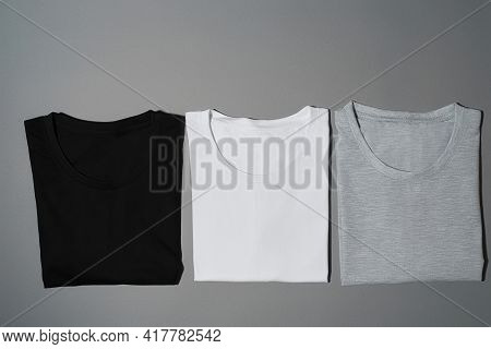 Top View Of Three Monochrome Black, White And Gray Cotton T Shirts Lying In A Row. Flat Lay Tees Tem