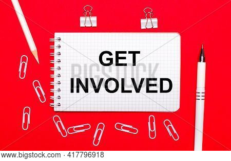 On A Red Background, A White Pen, White Paper Clips, A White Pencil And A Notebook With The Text Get
