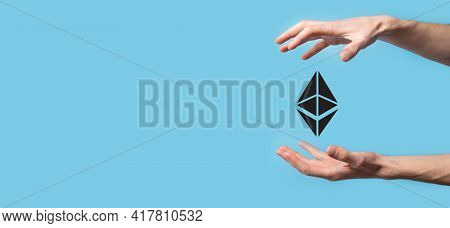 Male Hand Holding A Ethereum Icon On Blue Background. Ethereum And Cryptocurrency Investing Concept.