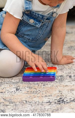Close Up Young Little Girl Sitting On The Modern Rug At Home Playing Poppit - New Fidget Toy, Popula