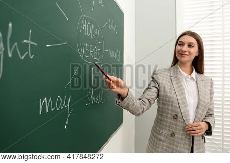 English Teacher Giving Lesson On Modal Verbs Near Chalkboard In Classroom