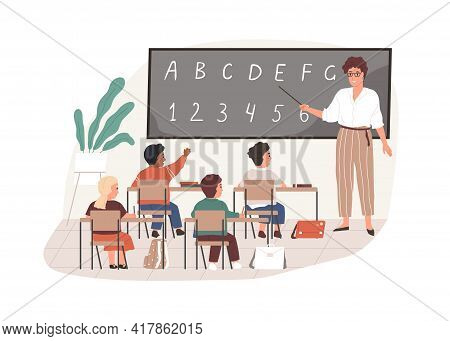 Young Teacher With Pointer At Chalkboard In Classroom. Elementary School Children Studying In Class 