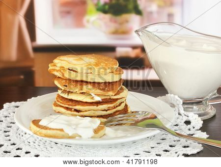 หวาน pancakes บนแผ่น ด้วยครีมเปรี้ยวบนโต๊ะในห้อง
