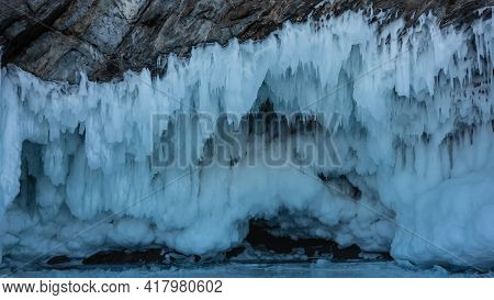 Icicles Hang From The Base Of The Rock In Several Rows, Like Lace Frills. Close-up. Stone And Ice Te