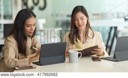 Two Female Office Workers Working On Their Project Together With Office Supplies In Meeting Room