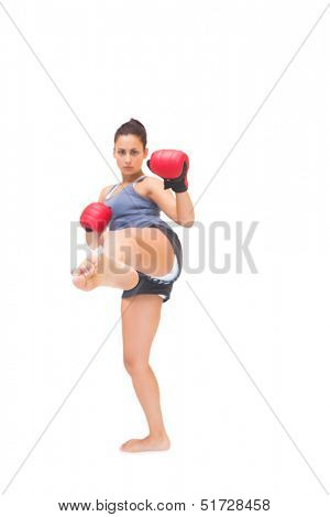 Stern sporty brunette kick boxing on white background