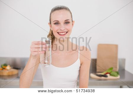 Happy young woman holding glass of water in the kitchen at home