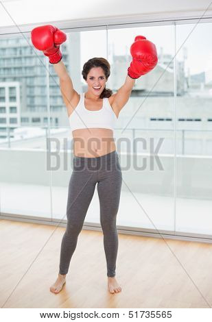 Sporty laughing brunette cheering with boxing gloves in bright room