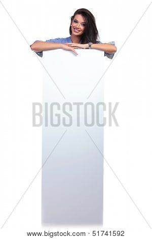 full length picture of a young casual woman standing behind an empty pannel and smiling for the camera. on white background