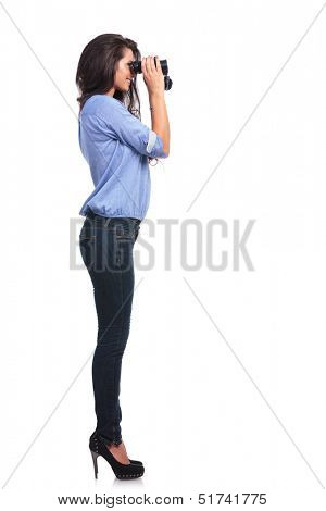 full length side view of a young casual woman looking away through binoculars. on white background