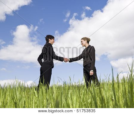 Two women standing in the grass shaking hands