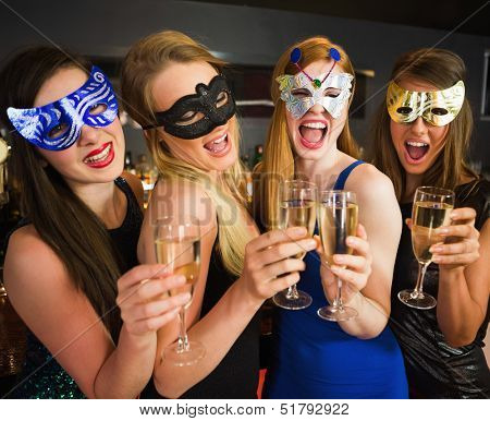 Attractive friends with masks on holding champagne glasses laughing at camera