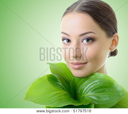 beautiful yoiung cheerful woman with green leaves near her face, care of nature concept, over green background