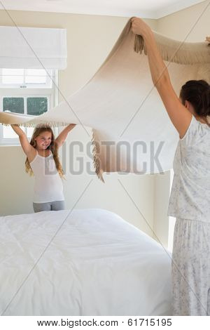 Mother and daughter making bed together in house