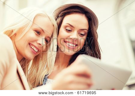 holidays and tourism concept - beautiful girls toursits looking into tablet pc in the city