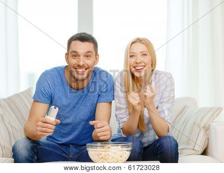 food, love, family, sports, entretainment and happiness concept - smiling couple with popcorn cheering sports team at home
