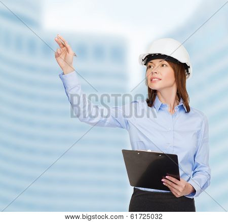 building, developing, consrtuction and architecture concept - smiling businesswoman in white helmet with clipboard pointing finger