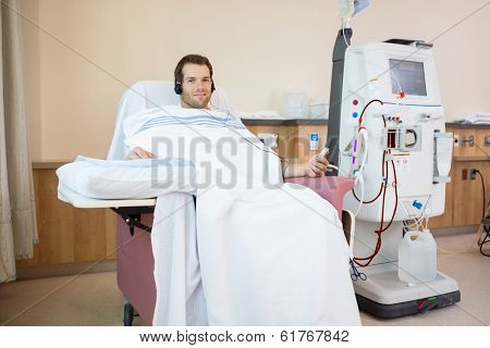 Portrait of young male patient listening to music while receiving renal dialysis treatment in hospital room