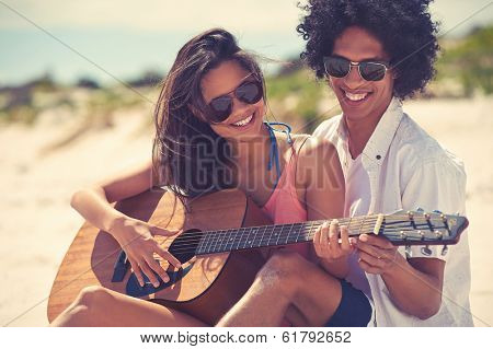 Cute hispanic couple playing guitar serenading on beach in love and embrace