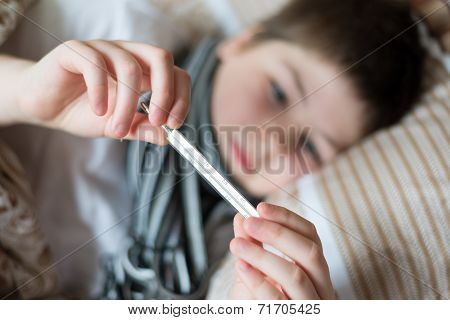 Sick Boy With Thermometer Lying In Bed