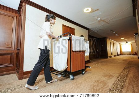 Hotel room service. female housekeeping worker with bedclothes linen in cart